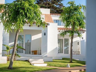 Bungalow bianco moderno dell'hotel con due alberi e prato verde in primo piano.