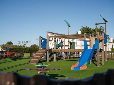 Parco giochi moderno per bambini con scivolo e struttura da arrampicata nel terreno dell'hotel sotto un cielo sereno.
