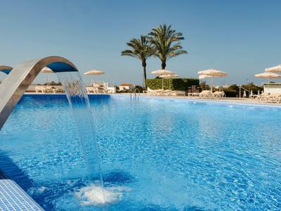 Piscina blu con cascata, ombrelloni bianchi e palme sullo sfondo.