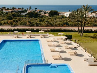 Area piscina con lettini, vista su prato, strada e mare sullo sfondo.