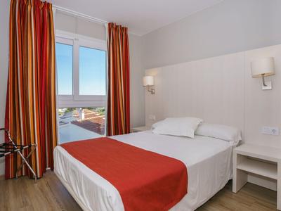 Camera d'hotel luminosa con letto matrimoniale, tende rosse e vista sul mare.