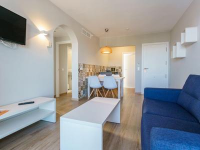 Soggiorno luminoso con divano blu, tavolino bianco, tavolo da pranzo e angolo cottura sullo sfondo.