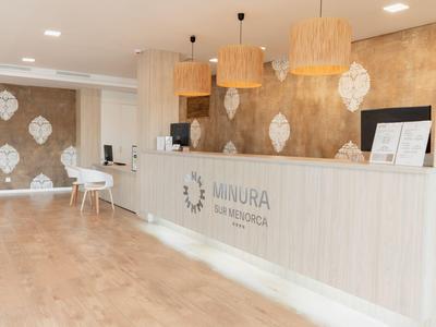 Area reception dell'hotel luminosa con pavimento in legno e banco reception bianco moderno.