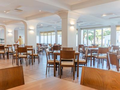 Sala da pranzo luminosa e moderna con tavoli e sedie in legno in un hotel con grandi finestre.
