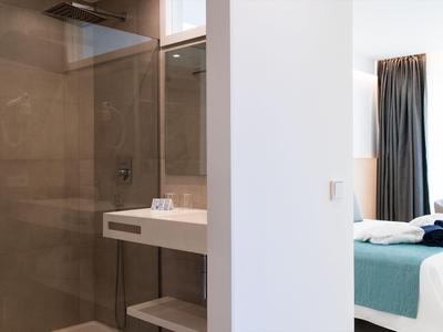 Espace salle de bain moderne d'hôtel avec douche en verre, lavabo et chambre adjacente.