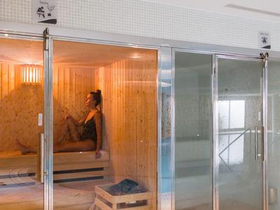 Femme se détendant dans un sauna avec des murs en bois et des portes coulissantes en verre.