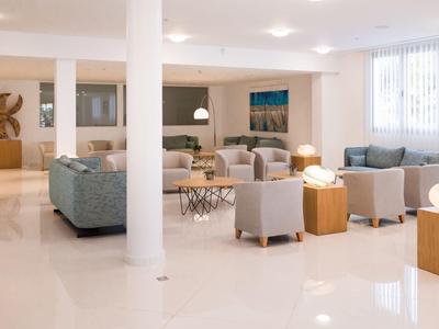 Salon d'hôtel lumineux avec fauteuils confortables, tables et grandes fenêtres.
