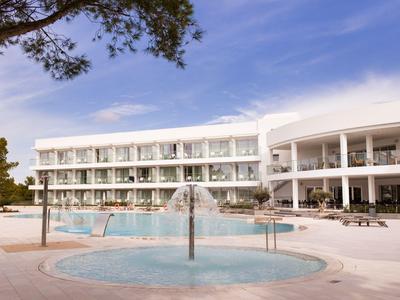 Complexe hôtelier moderne avec piscine et fontaine sous un ciel bleu.