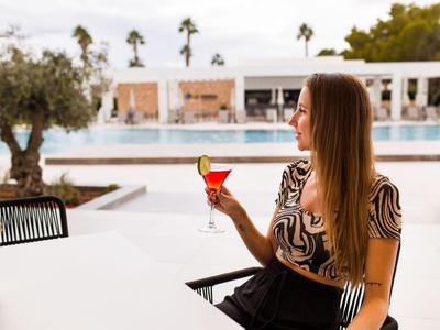 Femme avec cocktail près de la piscine dans un cadre hôtelier moderne avec des palmiers en arrière-plan.