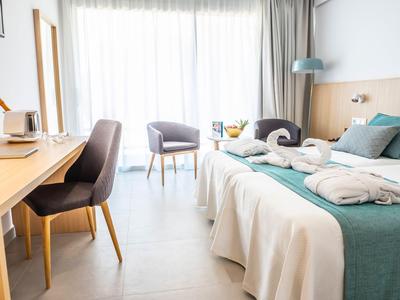 Chambre d'hôtel moderne avec lit double, bureau, fauteuils et balcon lumineux.