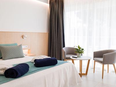 Chambre d'hôtel lumineuse avec lit double, deux serviettes et coin salon avec chaises et table.