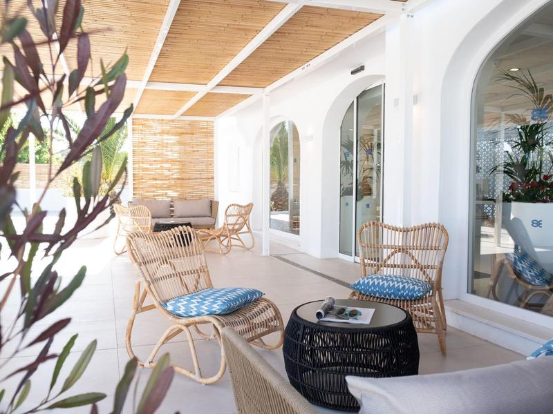 Terraza con sillas de mimbre, mesa de centro y ventanales en un hotel.
