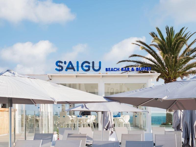 Bar de playa con sombrillas blancas, palmeras y vista al mar bajo cielo soleado.