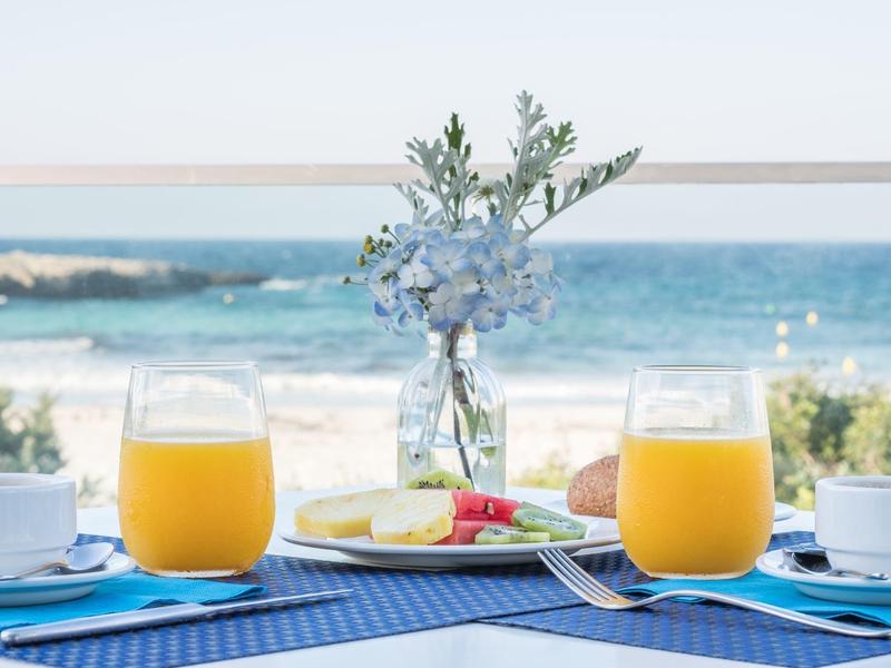 Mesa con jugo de naranja, flores y vista al mar en la playa