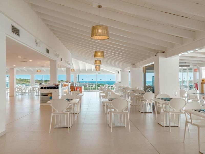 Amplio comedor de hotel luminoso con muebles blancos y vista al mar.