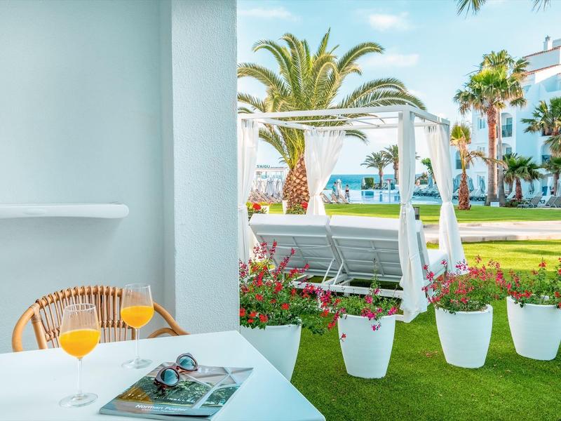 Vista desde una terraza con bebidas hacia un jardín con palmeras y edificios de hotel.