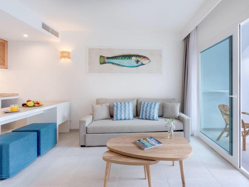 Sala luminosa con sofá, puerta al balcón y cocina moderna en diseño claro.