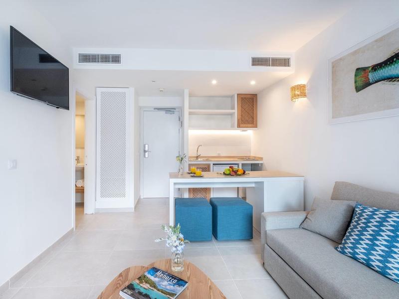 Sala de estar moderna con sofá, mesa de centro, área de comedor y televisor de pantalla plana en la pared.