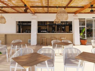 Espace extérieur lumineux avec plafond en bois, chaises transparentes et tables en bois dans un hôtel.
