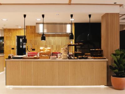 Comptoir de petit-déjeuner moderne en bois clair avec diverses nourritures et plantes sur fond sombre.