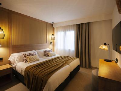 Chambre d'hôtel moderne avec lit double, murs en bois, éclairage chaleureux et fenêtre avec rideaux.
