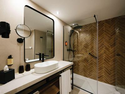 Salle de bain d'hôtel moderne avec carreaux en bois, grande douche et lavabo blanc.