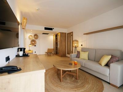 Espace chambre d'hôtel moderne avec canapé, table basse, TV et couleurs chaudes naturelles.