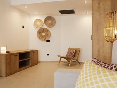 Chambre d'hôtel lumineuse avec meubles en bois, luminaires muraux et paniers décoratifs au mur.