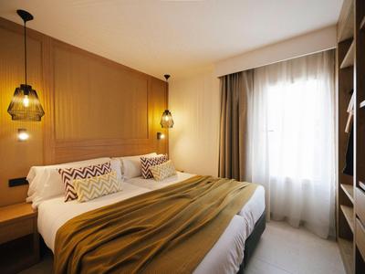 Chambre d'hôtel moderne avec grand lit, décor en bois chaleureux et lumière naturelle.