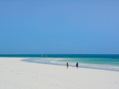 Weißer Sandstrand mit blauem Himmel und zwei Personen am Ufer.
