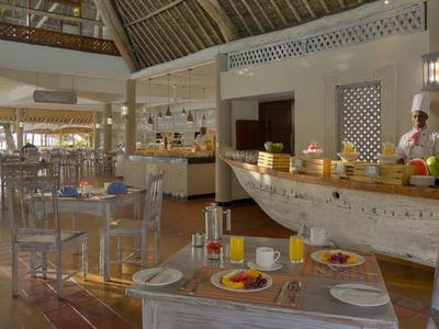 Helles Restaurant mit Holzboden, gedeckten Tischen und Buffet in Bootform an Wand mit großen Fenstern.