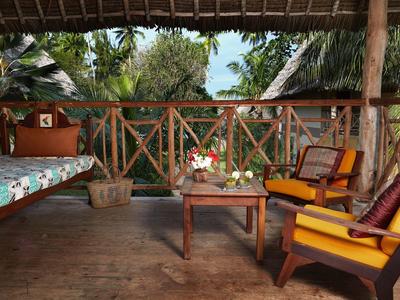 Gemütliche Terrasse mit Holzmöbeln, bunten Kissen und tropischer Pflanzenkulisse.