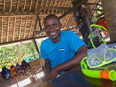 Hombre con camiseta azul sentado en una mesa con equipo de snorkel en una cabaña abierta.