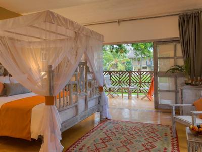 Gemütliches Schlafzimmer mit Himmelbett, orangefarbener Bettdecke und Zugang zu Balkon mit Grün.