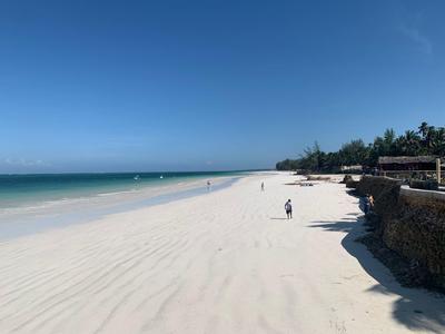 Breiter weißer Sandstrand mit blauem Himmel, ruhigem Meer und wenigen Spaziergängern.