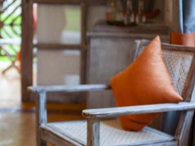 Stuhl mit orangenem Kissen, Holztisch davor mit Obstkorb aus Äpfeln und Trauben.