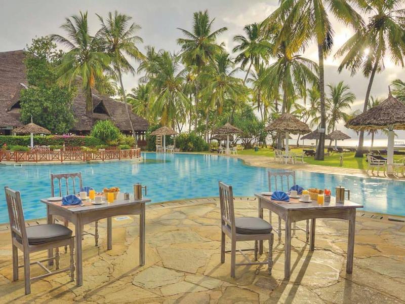 Tische mit Stühlen am Pool in tropischem Hotelresort bei Sonnenuntergang.