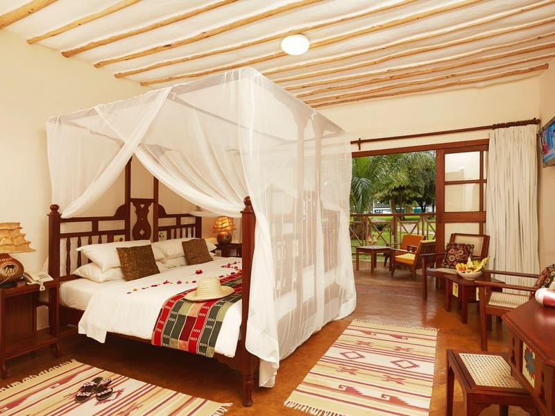 Hell eingerichtetes Schlafzimmer mit Holzmöbeln, Himmelbett und offenem Blick auf Terrasse und Garten.