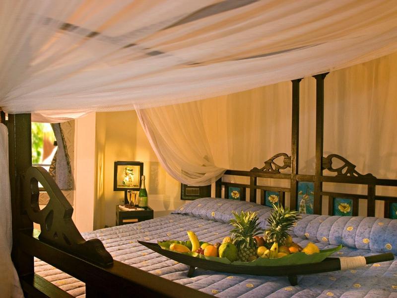 Gemütliches Schlafzimmer mit Holzbett, Moskitonetz und Dekoschale mit Früchten.