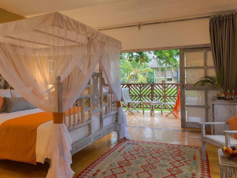 Gemütliches Schlafzimmer mit Himmelbett, orangefarbener Bettdecke und Zugang zu Balkon mit Grün.