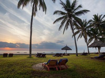 Sonnenuntergang am Strand mit Palmen und Liegestühlen unter klarem Himmel.