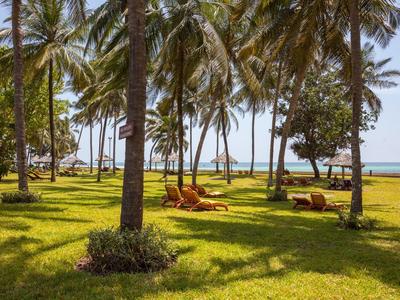 Sonnige tropische Grünfläche mit Palm Bäumen und Liegestühlen am Meer