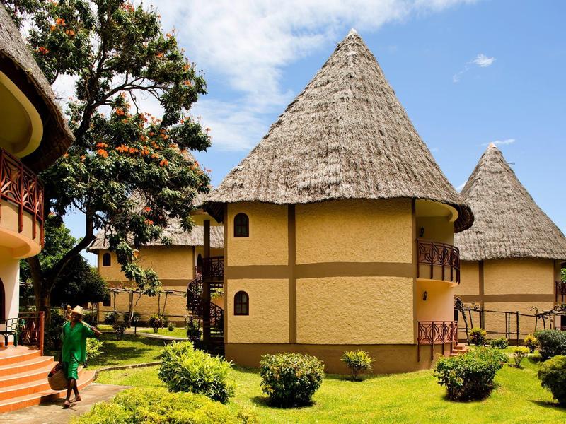 Capanne rotonde tradizionali con tetti di paglia in un giardino ben curato con sole.