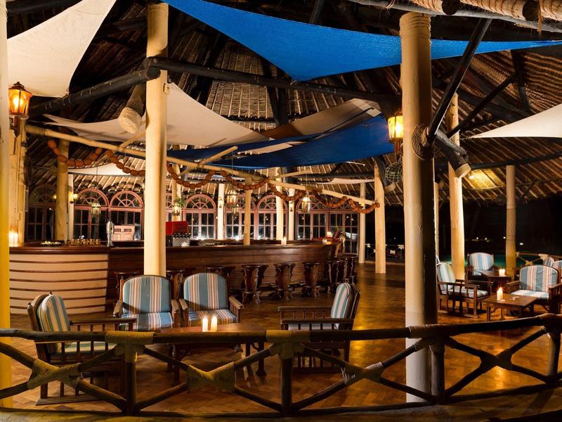 Bar accogliente con mobili in legno e vele solari blu in un resort tropicale aperto.