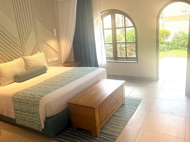 Camera d'hotel luminosa con letto grande, mobili in legno e vista sul giardino attraverso finestre ad arco.