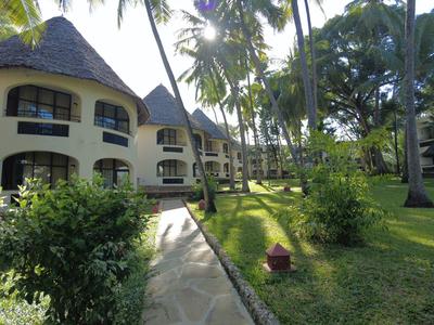 Budovy resortu s doškovými střechami obklopené palmami a zelenými trávníky.