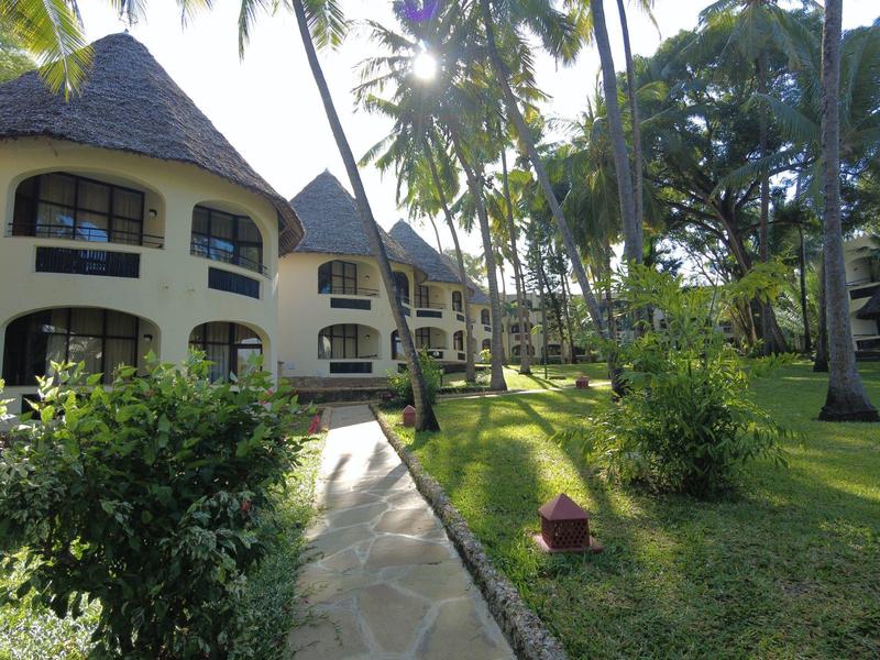 Budovy resortu s doškovými střechami obklopené palmami a zelenými trávníky.