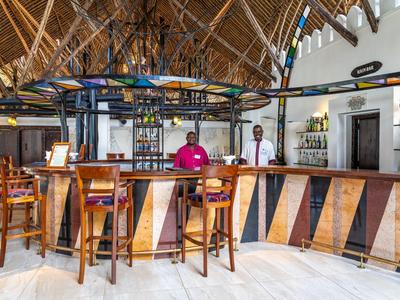 Moderní hotelový bar s dřevěnými židlemi a tropickou střechou z palmových listů.