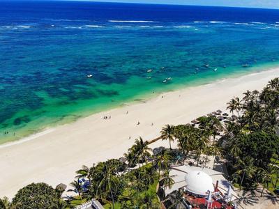 Pohled na bílou písečnou pláž s tyrkysovou vodou a palmami podél pobřeží.