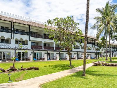 Dvoupodlažní hotelová budova s balkony a zeleným trávníkem se stromy palem v popředí.